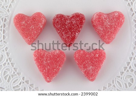 Single red and four pink sugar coated heart candies set on a white doily.