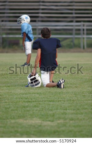 A young football player watches a game waiting to enter from the sidelines.