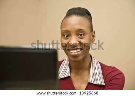 An attractive African American office worker, information technology specialist or business woman seated at a computer.