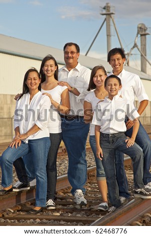 A family of six photographed at sunset in an industrial location featuring railroad tracks.