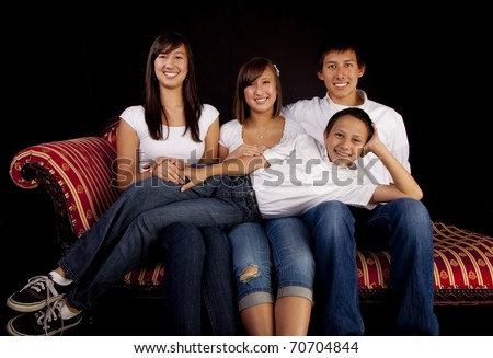 Teen children from a multicultural American family of six in a seated studio portrait with a black background.