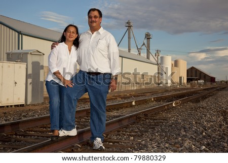 A multicultural couple photographed at sunset in an  industrial location featuring railroad tracks.