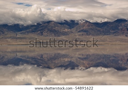 A reflection of mountains and dramatic sky on the rarely water filled valley in Badwater, Death Valley National Park, California.