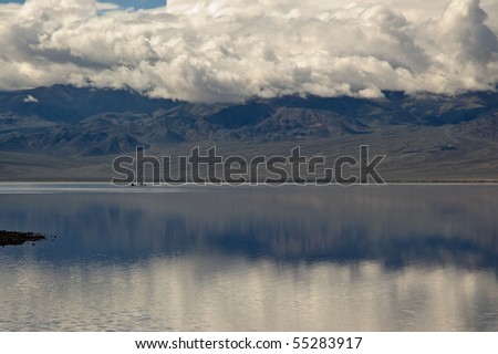 Two people canoe beneath the mountains and clouds in the lake at Badwater, Death Valley National Park, California.
