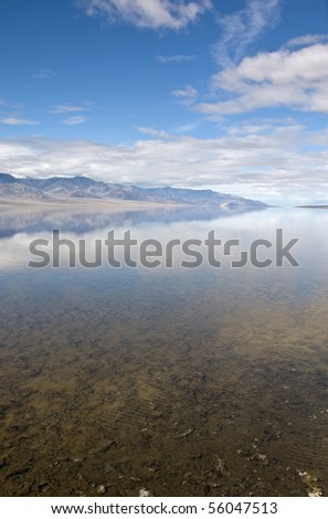 A reflection of mountains and dramatic sky on the rarely water filled valley in Badwater, Death Valley National Park, California.