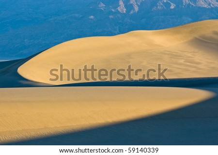 First light hits the sand dunes on Mesquite Flat showing curved patterns of light and shadow in Death Valley National Park, California.