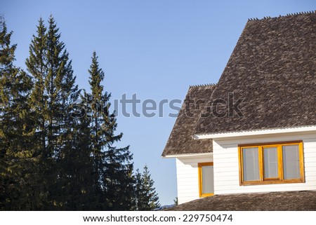 An lateral view at one attic window of a small wooden house in the mountains in autumn. Roof detail can be seen, as well as a clear, blue sky.