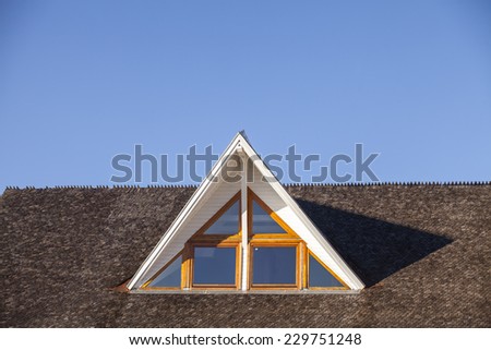 An upwards view at a attic window. Roof detail can be seen, as well as a clear, blue sky.