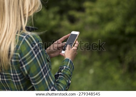 Beautiful blonde woman using mobile smart phone in a forest