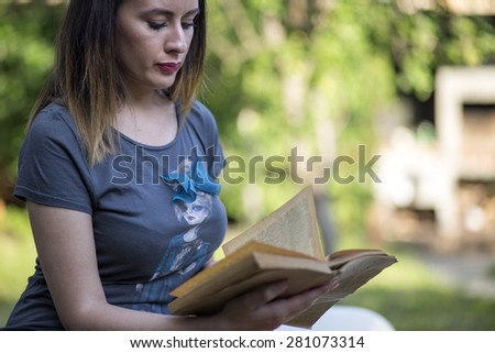 Beautiful girl in blue blouse read a book, against green of summer park.