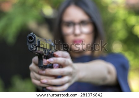 Close up Young Pretty Woman Pointing a Gun at the Camera with both Hands