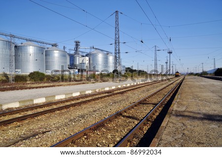 Group of silos filled with cereal grain against blue sky.Nearby railway lines and train