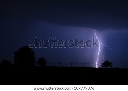 Lightning Strike at Night - Lightning strike lighting up the night sky and creating silhouettes of a power line and trees in the countryside.