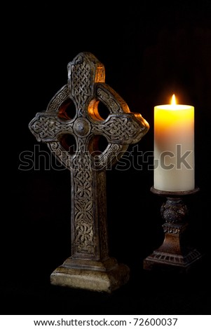 Celtic cross, illuminated by natural light, and a glowing candle on a black background