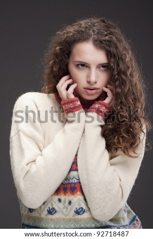 Girl in a colorful sweater looking off camera holding her hands to her cheeks.