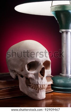 Grim looking human skull set on a few books lit by a retro desk lamp.