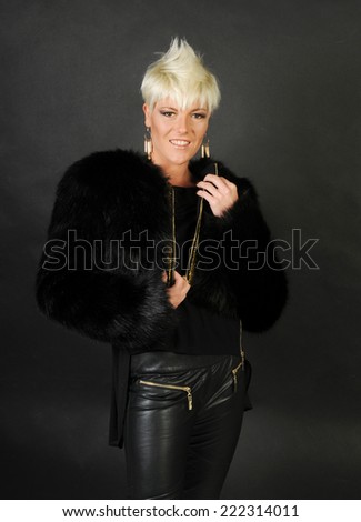 a portrait of a trendy short haired model unzipping her black fur coat isolated on black background