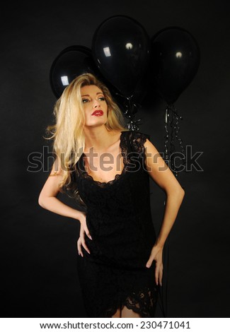 Full size portrait of beautiful sensual blond lady wearing cocktail lace black dress and a perfect evening make up with red lipstick looking up on black background with black balloons