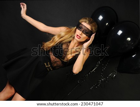 Young beautiful slim girl wearing black lace sensual top and black skirt with evening make up and black lace band on her eyes posing with black balloons and making scared face on black background