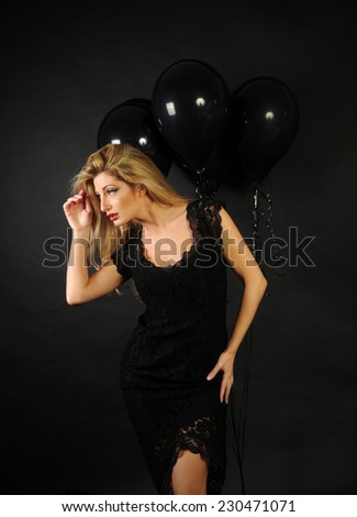 Full size portrait of beautiful sensual blond lady wearing cocktail lace black dress and a perfect evening make up with red lipstick posing in dolly poses on black background with black balloons