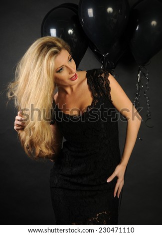 Full size portrait of beautiful sensual blond lady wearing cocktail lace black dress and a perfect evening make up with red lipstick posing looking away on black background with black balloons
