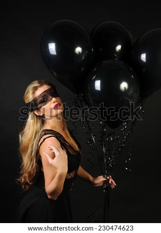 Young beautiful sensual slim girl wearing black lace sensual top and black skirt with evening make up and black lace band on her eyes posing and playing with black balloons on black background