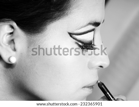 close up profile portrait of a Young girl finishing scenic make up and putting a lip pencil in black and white