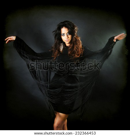 portrait of a beautiful young latin woman wearing black dress with long granges moving her arms up and down if she were Flying isolated on black