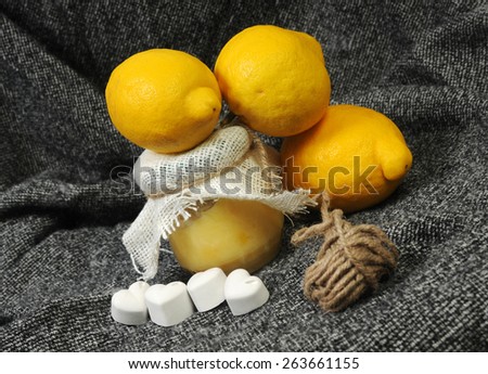 still life with a lemon marmalade jar and bright yellow lemons decorated with chalk hearts and linen on grey background