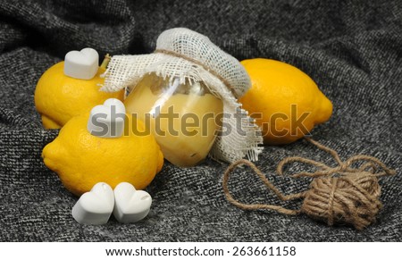 close up still life with a creamy lemon curd jar and bright yellow lemons decorated with chalk hearts and linen on grey background