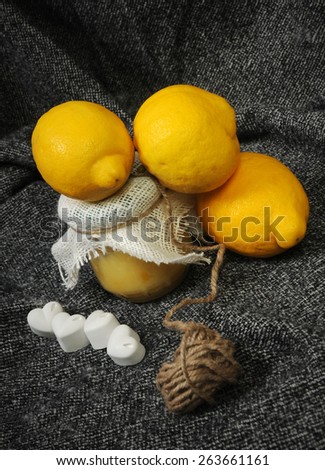 creamy lemon curd jar decorated with linen and rope with a lemon pyramid and white chalk hearts still life on gray background