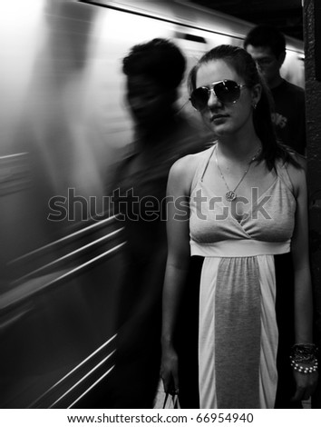 a young girl in front of the moving train and crowd in the subway monochrome