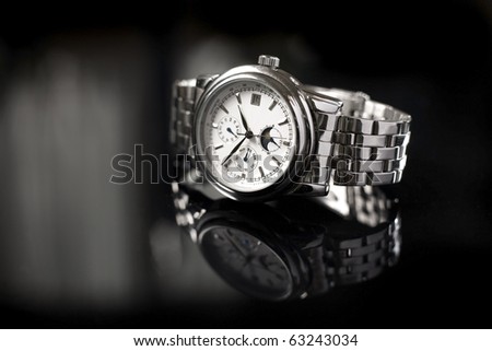 A silver coloured stainless steel watch for men on a reflective black background.