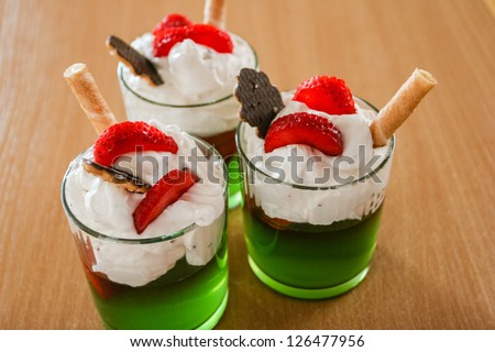 Green jello with whipped cream,strawberries, chocolate and waffle tubes in glass on a table.