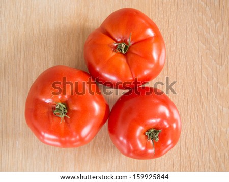 Three red tomatoes on wooden cutting board