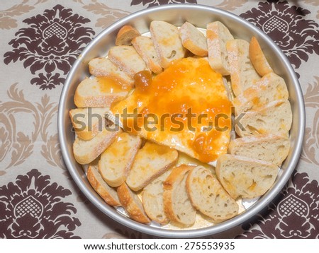 Large piece of brie cheese topped with jam and served with sliced bread.