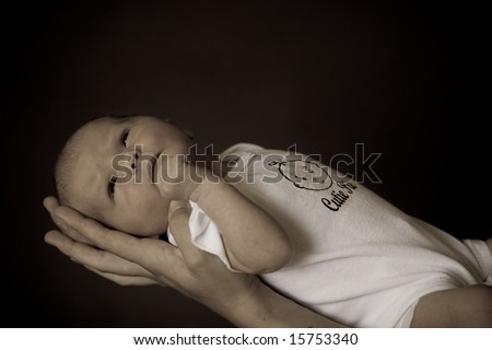 Little 7 days old baby lying securely on mom\'s arms, against a black background