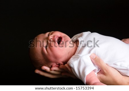 Little 7 days old baby lying securely on mom\'s arms, against a black background