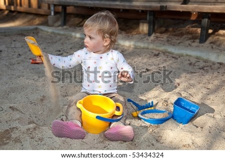 Cute Caucasian baby girl playing with the sand in sandpit.