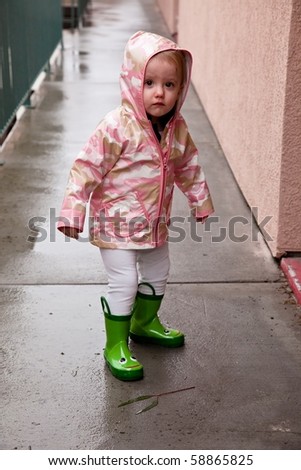 Cute caucasian baby girl wearing pink raincoat and green rubber boots.