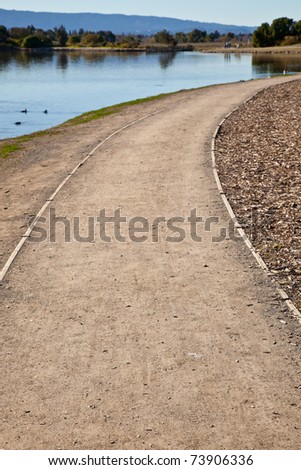 GRavel road in a park winding right from the lake shore.