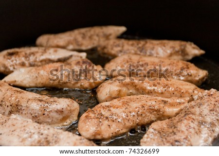 Frying juicy tenderloin chicken breasts on black pan.