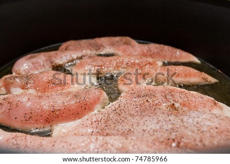 Frying juicy tenderloin chicken breasts on black pan.
