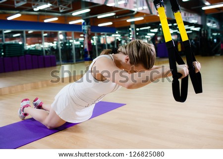 Young attractive woman does suspension training with fitness straps in the gym\'s studio