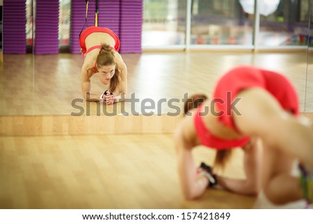Young attractive woman does core abs crossfit training with trx fitness straps in the gym\'s studio, reflected in mirror