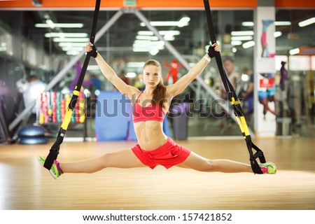 Young attractive woman does splits crossfit stretching with fitness trx straps in the gym\'s studio