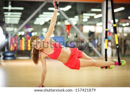 Young attractive woman does core abs crossfit oblique training with fitness trx straps in the gym\'s studio