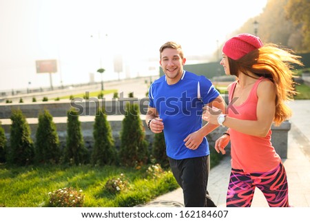 Young couple of athletes running on the empty street in the morning. The woman is looking at her partner. Everyone is smiling.