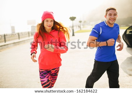 Young couple of athletes running on the empty street in the morning. The fog gives depth and dimensional look to the shot. Everyone is smiling.