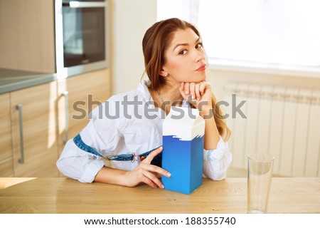 Young beautiful woman sitting at the table with a carton of milk and empty glass